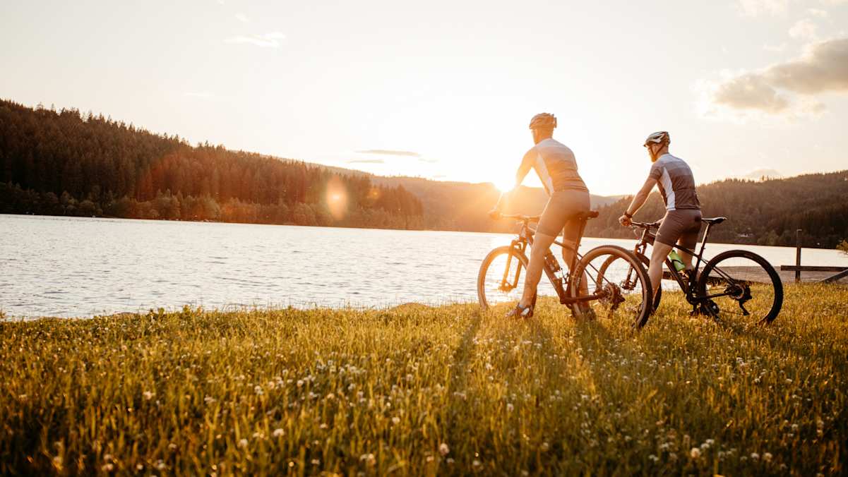 Zwei Mountainbiker genießen den Sonnenuntergang mit Blick auf einen See.
