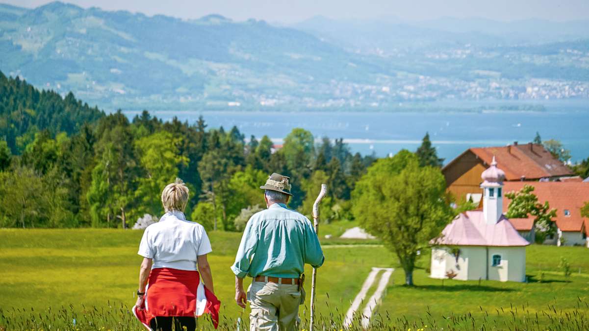 Ein Mann und eine Frau wandern in Scheidegg mit Blick auf den Bodensee.