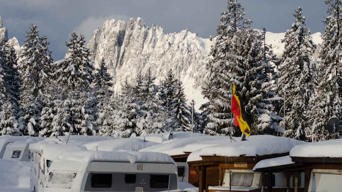 Auf dem Camping Jaunpass im Berner Oberland stehen die schneebedeckten Wohnwagen im Winter direkt vor der imposanten Bergkulisse der Gastlosen.