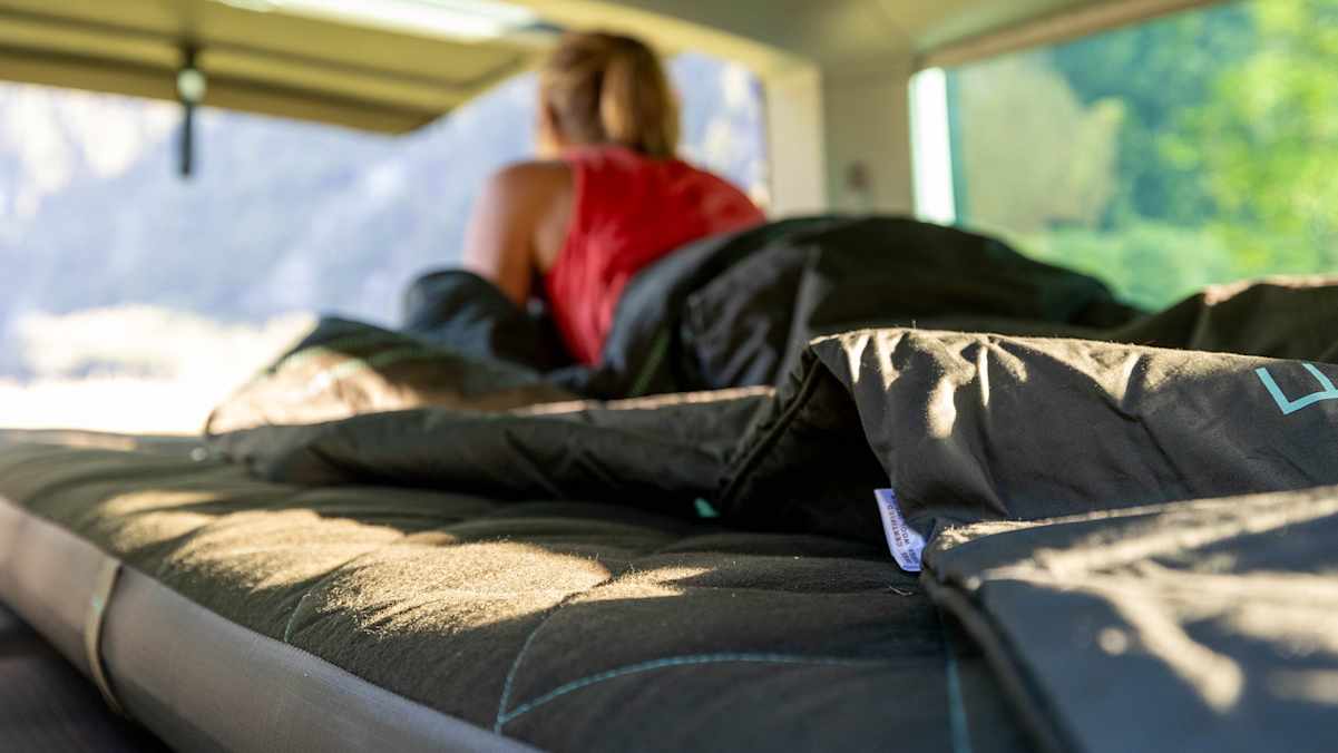 Eine Frau liegt in ihrem Van auf einer Matratze.