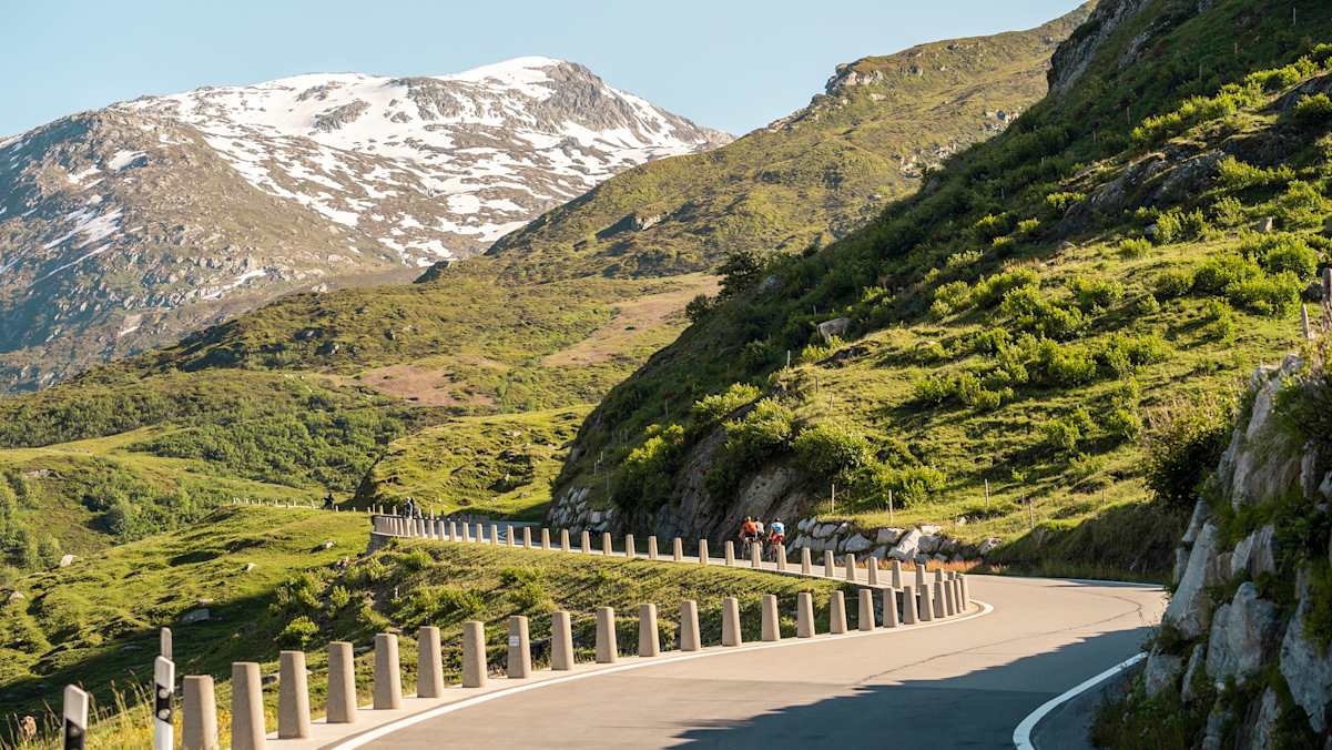 Schneeberge, grüne Hügel und Radfahrer auf dem Asphalt im Sommer.