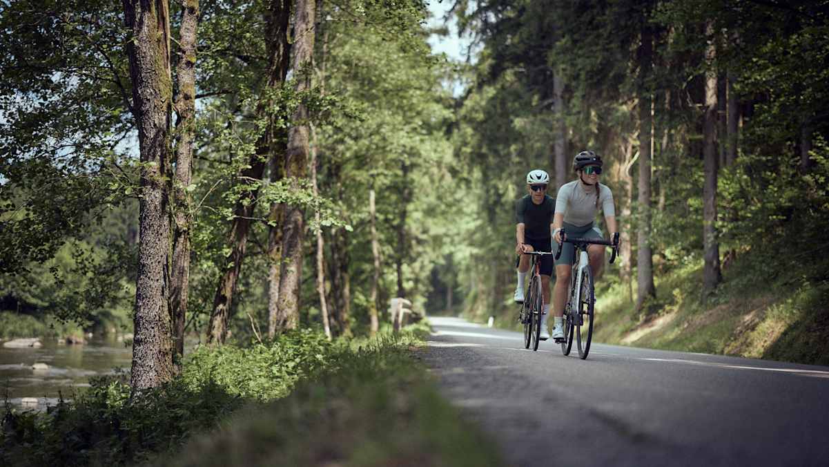 Eine Frau und ein Mann fahren im Wald neben einem Fluss Fahrrad