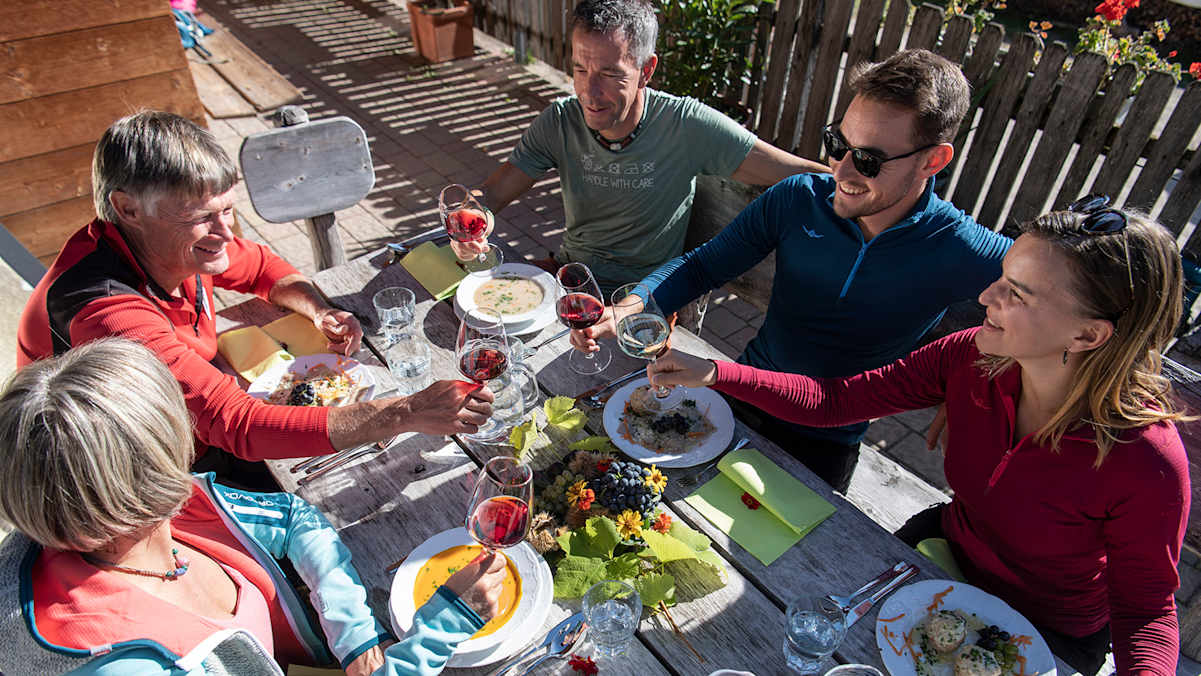 Fünf Personen sitzen um einen Tisch und prosten sich mit Wein zu.