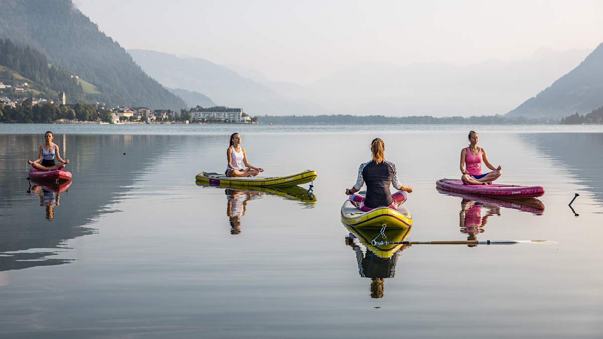 Vier Frauen sitzen mit verschränkten Beinen auf ihren SUPs und meditieren auf dem See.