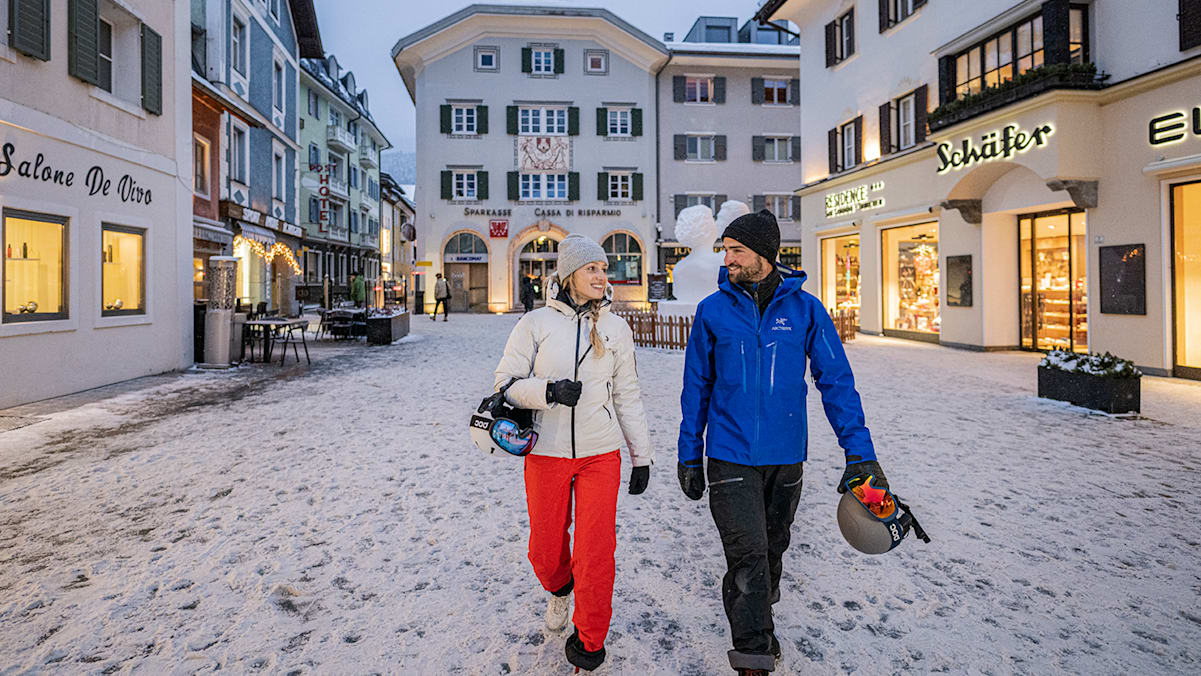 2 Personen in der Stadt Innichen im Winter mit Skiausrüstung.