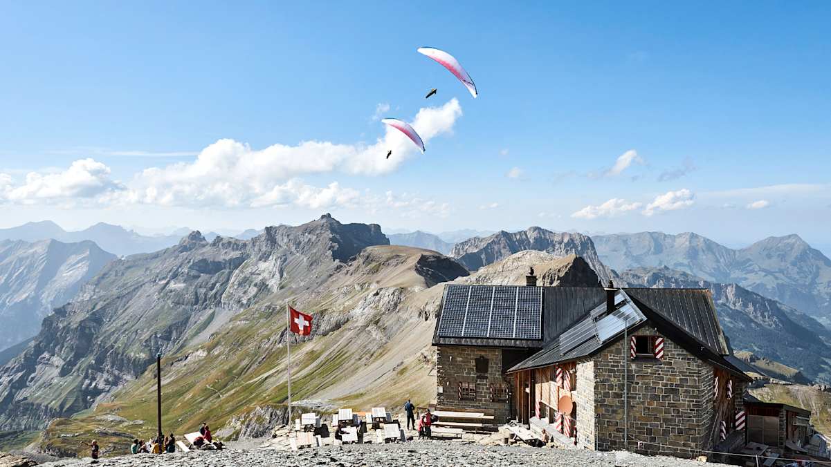 Eine Hütte mit zwei Paragleitern im Hintergrund.