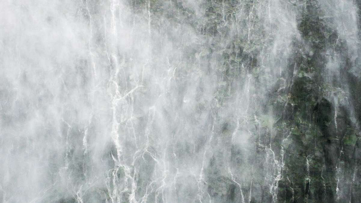 Gischt vor steilem Felshang mit Wasserfällen