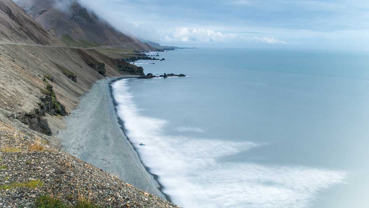 Schroffe Berge mit Kiesstrand und grau-blauem Meer