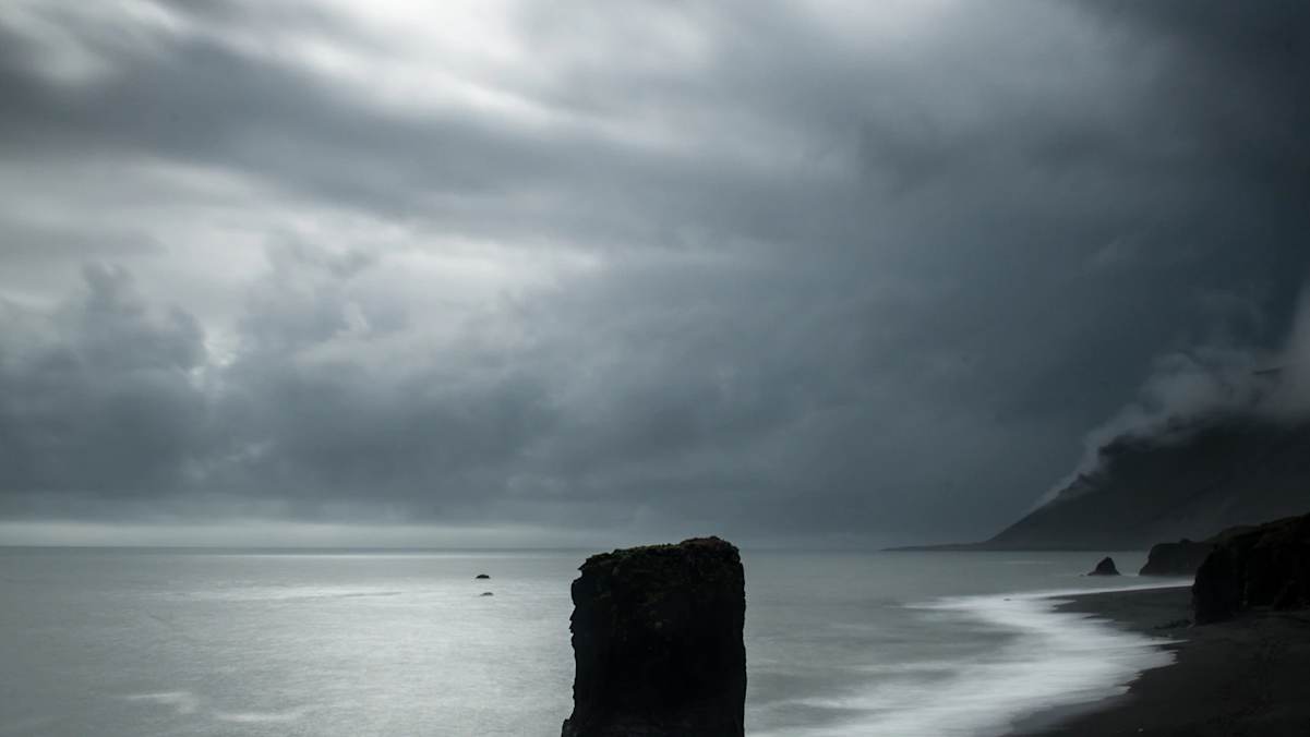Ein einsamer Felsturm im Meer am schwarzen Strand