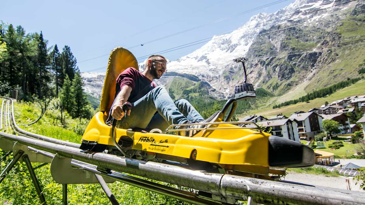 Person fährt auf einem gelben Sommerbob die Rodelbobbahn im Saas-Tal hinunter