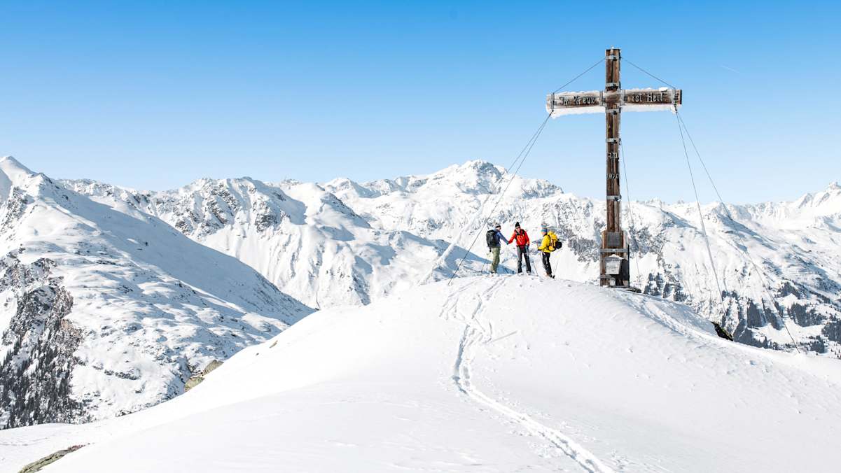 Drei Tourengeher beim Gipfelkreuz
