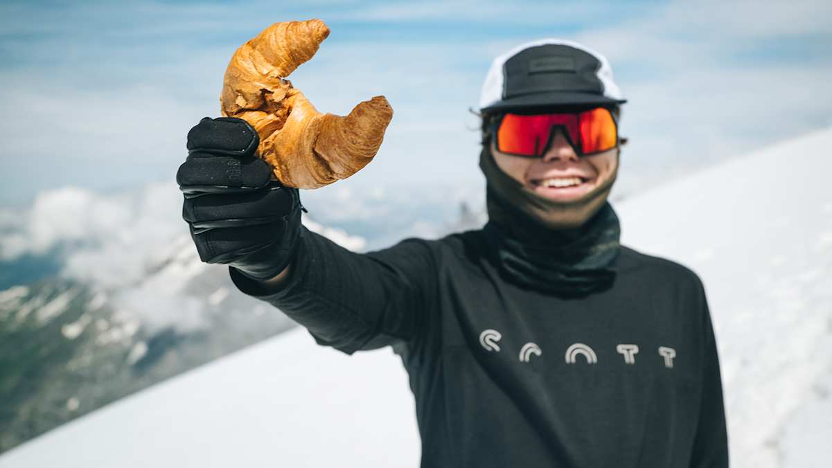 Tobias Renggli auf seiner Tour zu den höchsten Punkten aller Schweizer Kantone – mit einer Vorliebe für knusprige Gipfeli, das er auf dem Bild in die Kamera.