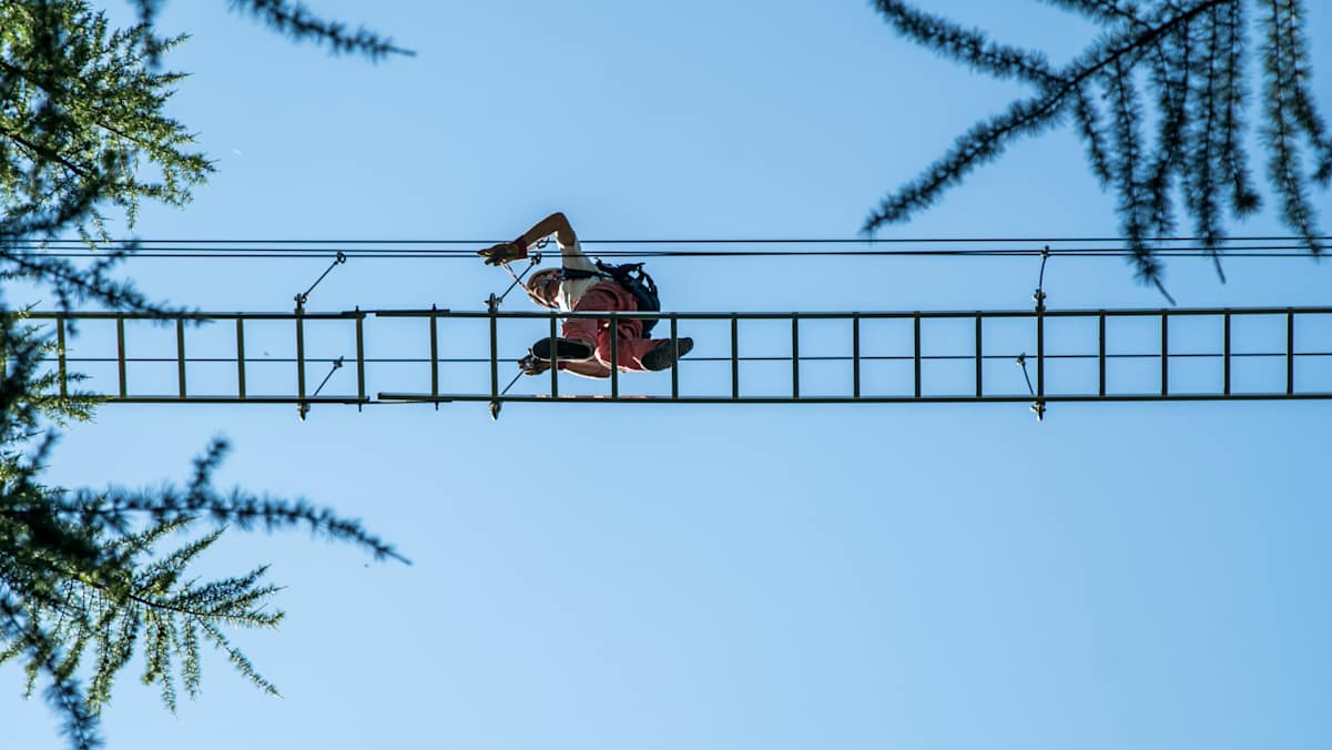 Person im Klettersteigset auf einer Drahtseilleiter von unten mit blauem Himmel im Hintergrund