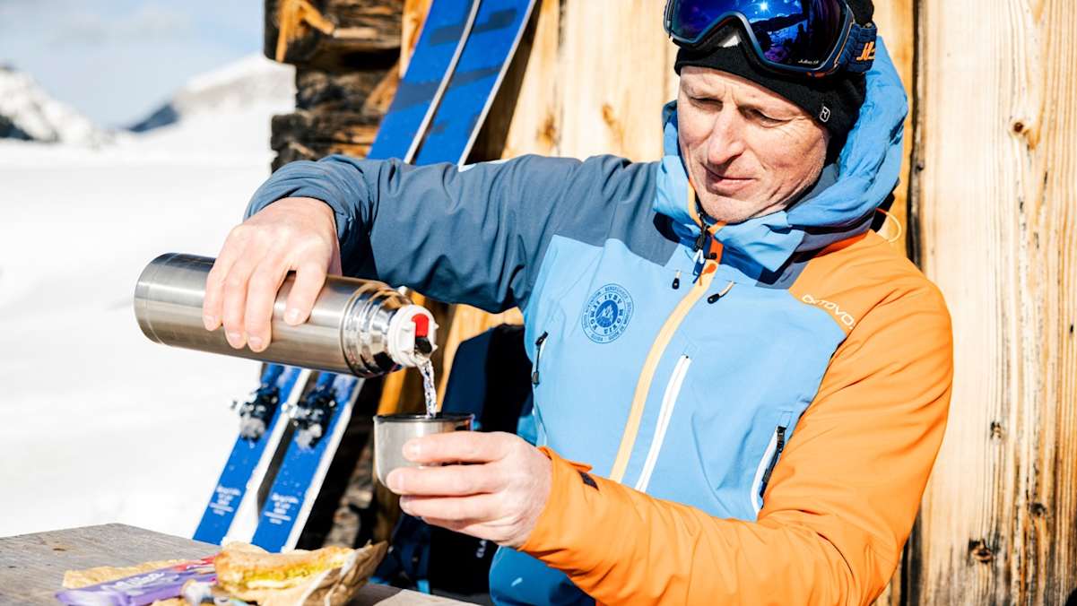 Mann trinkt Tee vor Hütte im Winter