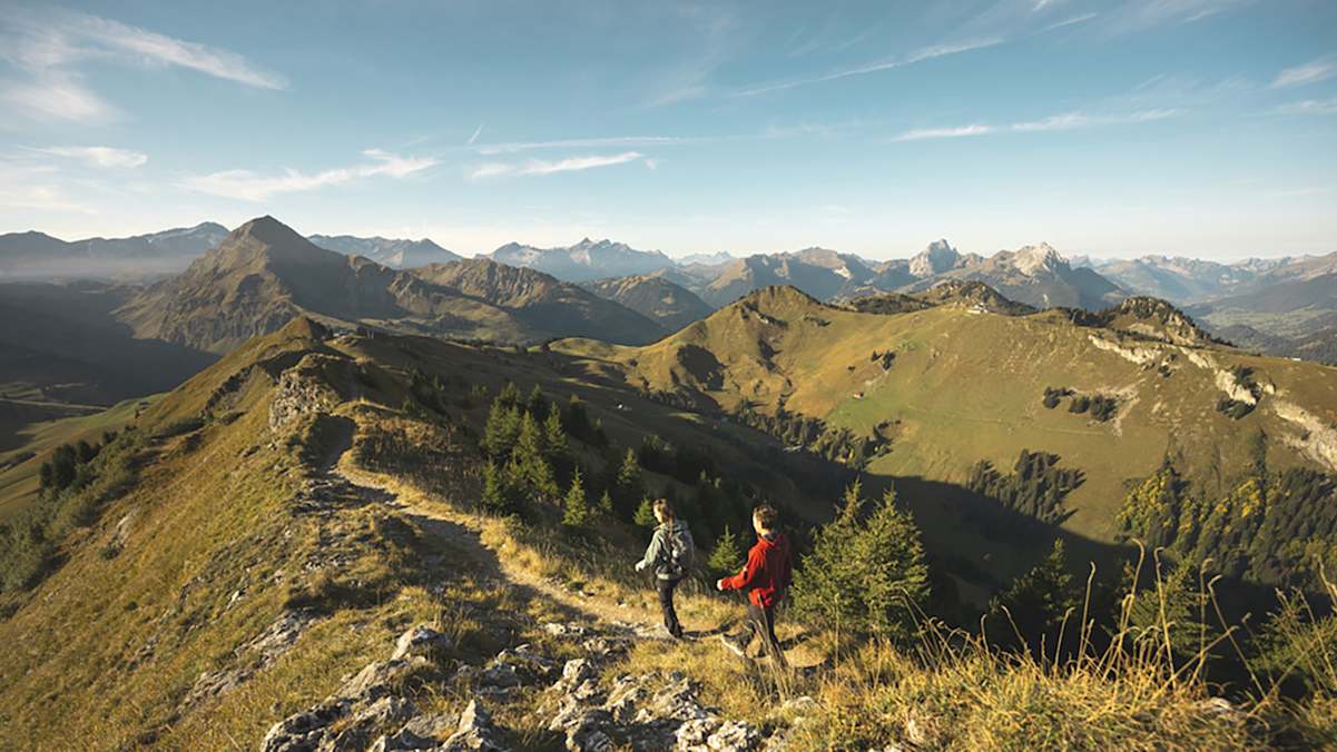 Wanderer auf einem Berggrat in der herbstlichen Alpenlandschaft von Gstaad mit Blick auf die umliegenden Gipfel.