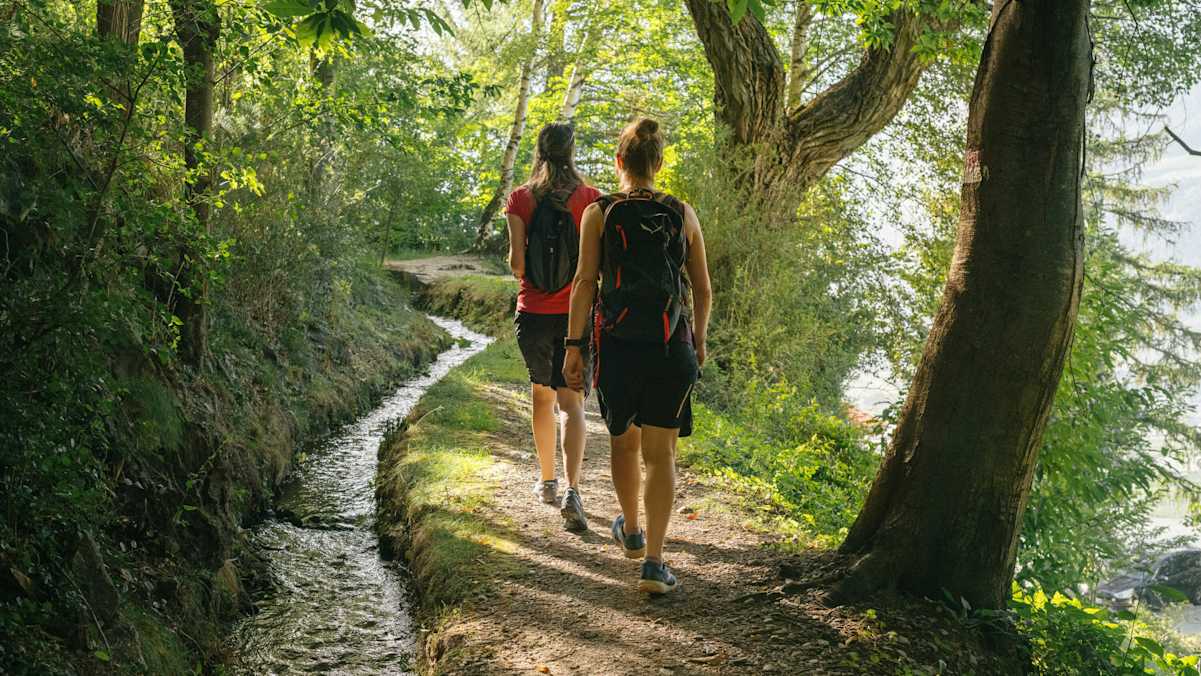 zwei Wanderinnen gehend entlang eines Waalweges in Südritol im Wald