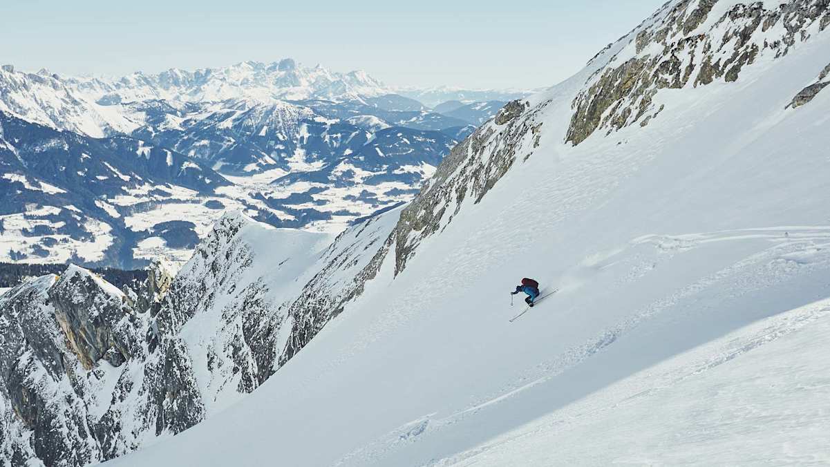 Ein Skifahrer bei der Abfahrt in einer Rinne, dahinter der Alpenhauptkamm.