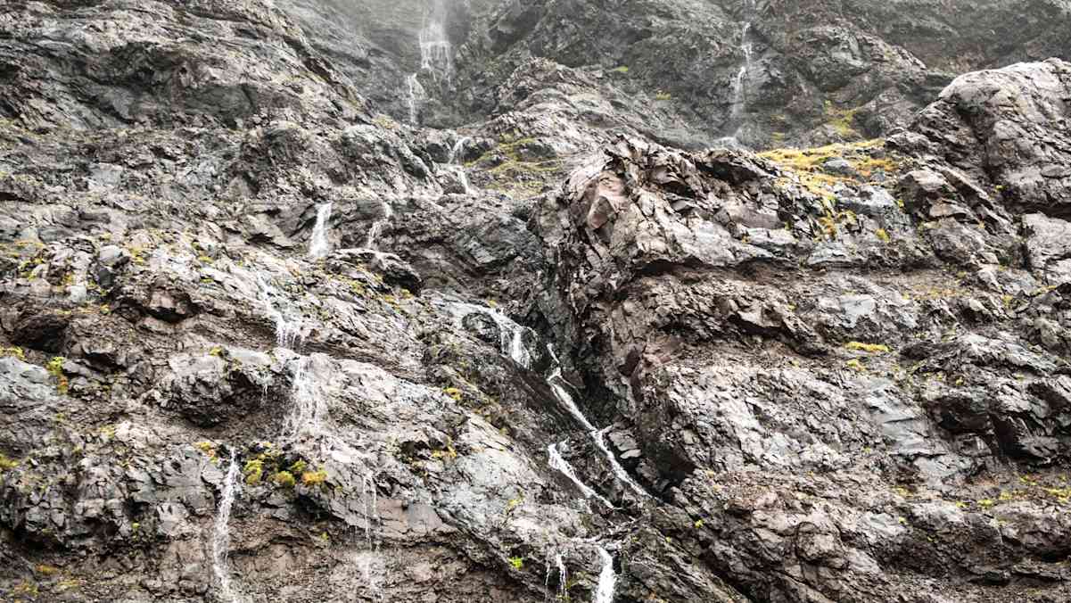 Karges Gestein und kleine Wasserfälle vor nebligem Himmel