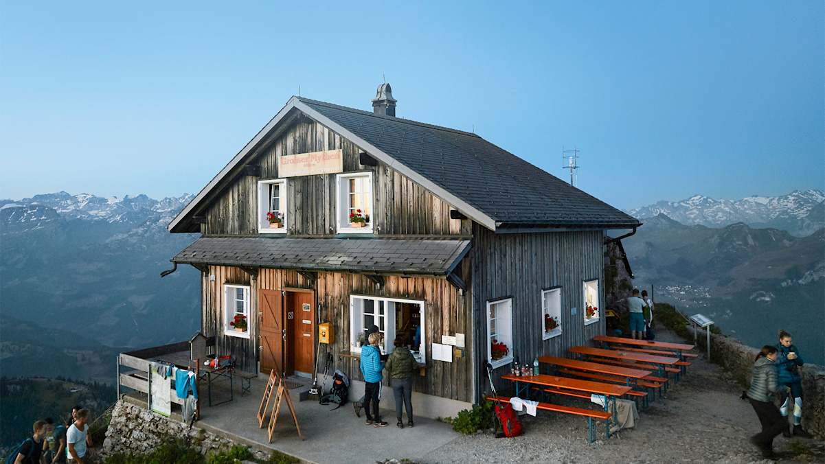 Ein Berggasthof bei Sonnenaufgang, dahinter die Berge.