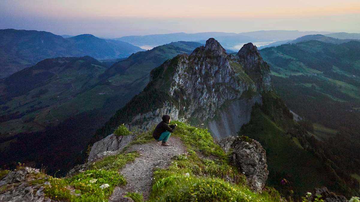 Eine Frau wartet vor wunderschönem Panorama auf den Sonnenaufgang.