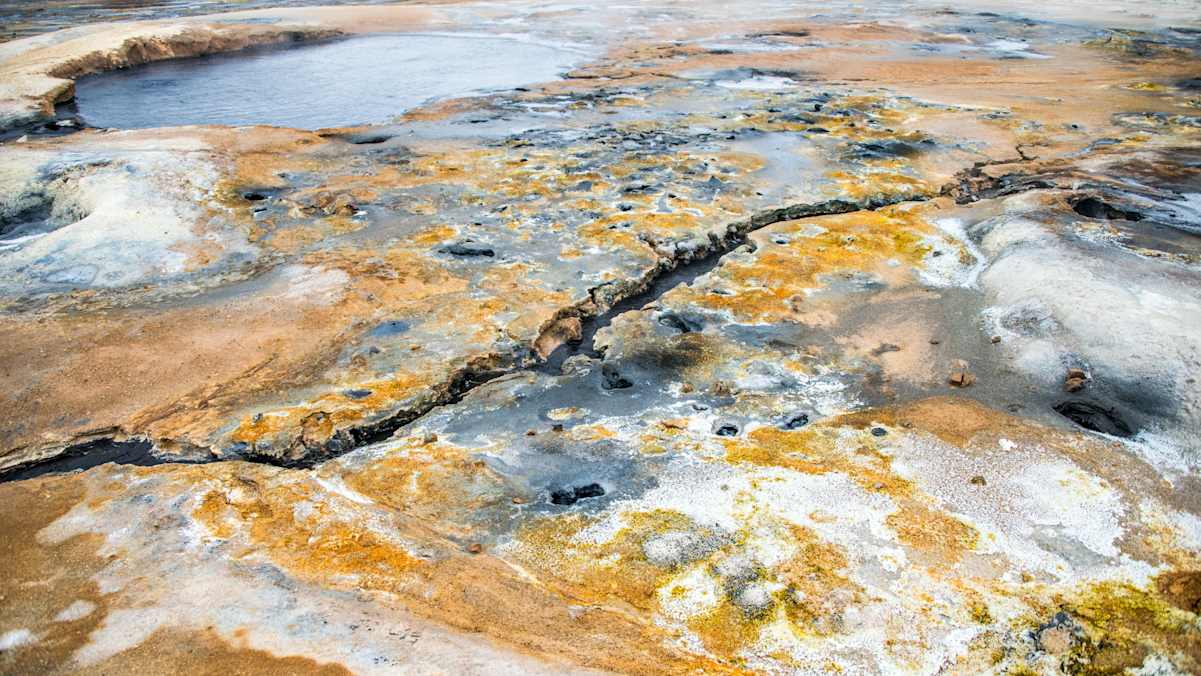 Gelb-Schwarzes Gestein mit Wasserbecken und kleinen Flüssen am Námafjall - Ort mit erhöhter vulkanischer Aktivität