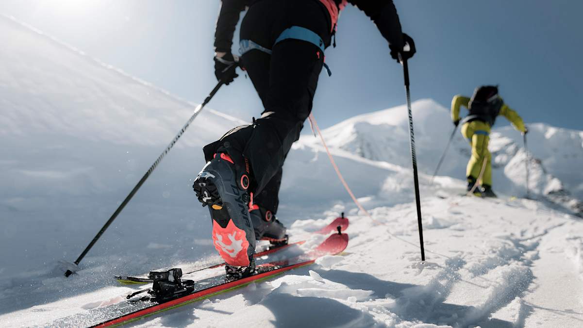 Skitourengeher mit Dynafit Blacklight-Ausrüstung beim Aufstieg durch tiefen Schnee im Hochgebirge bei Sonnenschein.