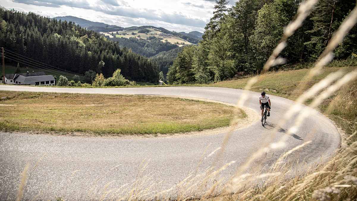 Radfahrer in weiter Kehre im Mühlviertel, umgeben von Hügeln und Waldlandschaft.