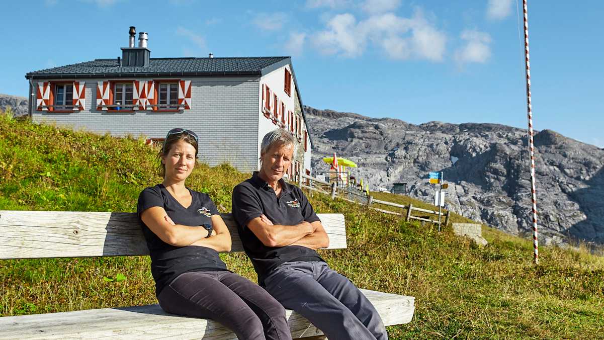 Die Hüttenbetreiber sitzen auf einer Bank vor der Hütte.