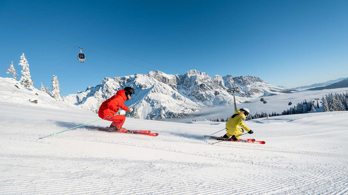 2 Skifahrer auf der Piste fahren den Hang herunter.