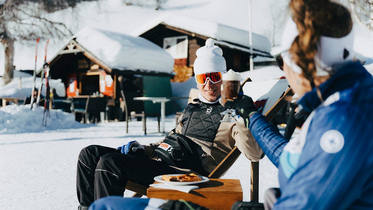 Ein Paar sitzt im Schnee und trinkt heiße Schokolade.