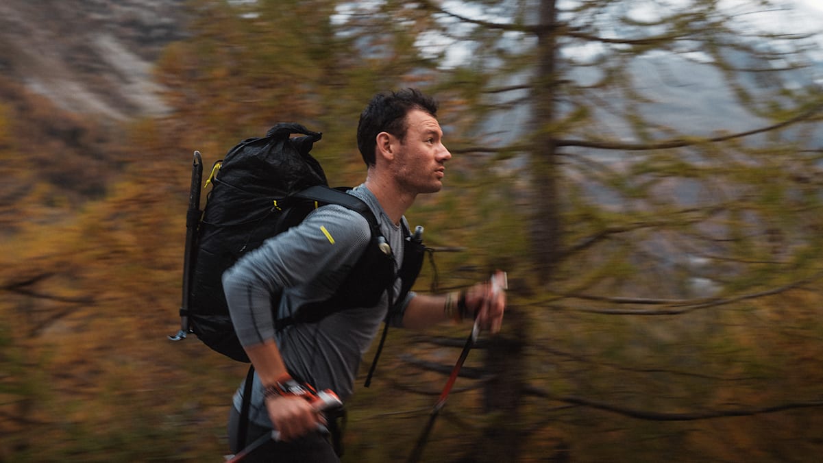 Ein Sportler im Wald mit Walkingstecken und Rucksack.