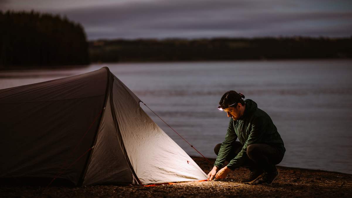 Manns schlägt in der Dämmerung ein Zelt auf und beleuchtet die Situation mit der Supreabeam V7.