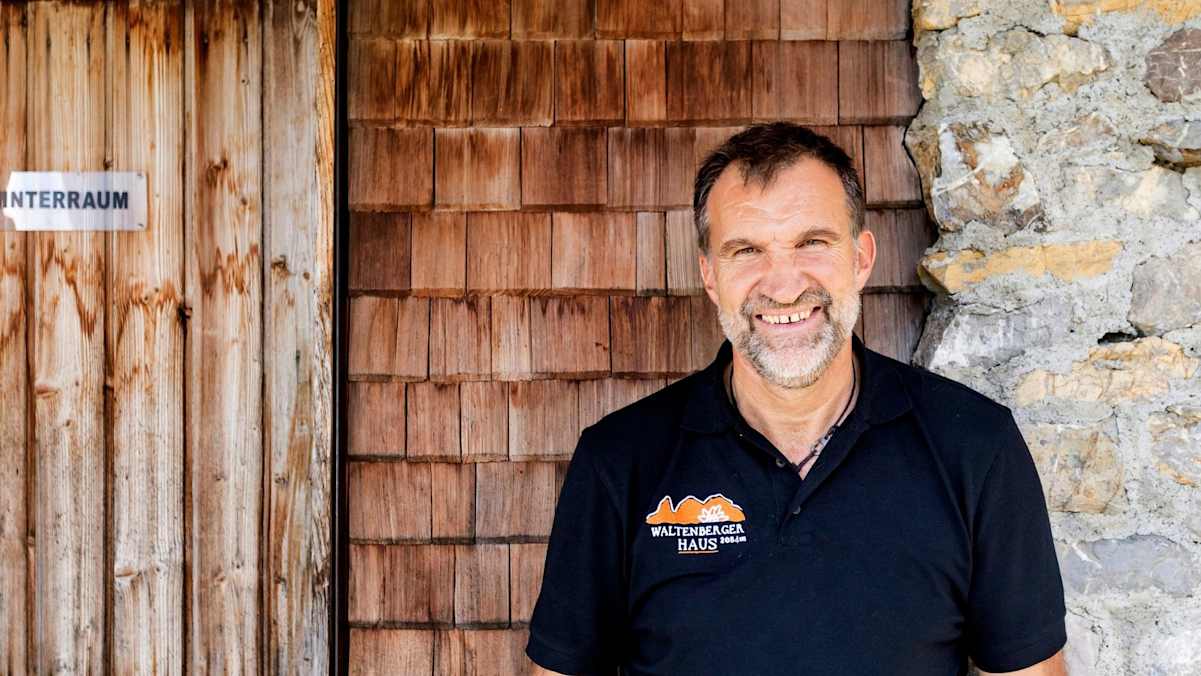 Ein Portrait des Hüttenwirts Markus vor einer Holzschindelwand