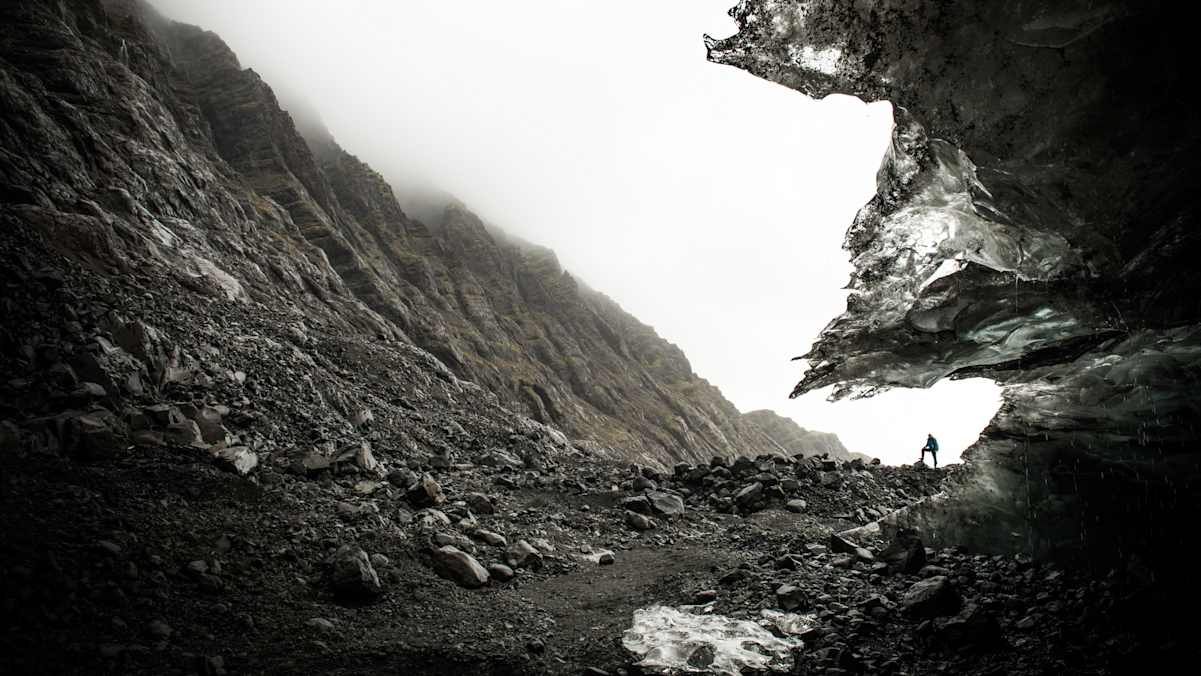 Mensch steht in Trogtal aus dunklem Gestein vor weißem Himmel
