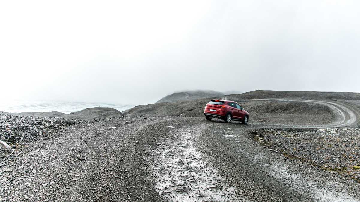 Rotes Auto auf isländischer Bergstraße bei nebligem Wetter