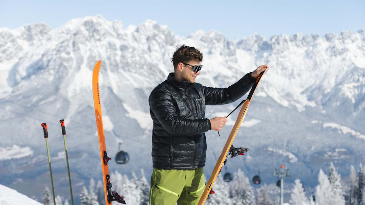 Ein Skitourengeher zieht in der Region Wilder Kaiser seine Felle von den Tourenskiern. Im Hintergrund die markante, tief verschneite Felskulisse des Wilden Kaisers.