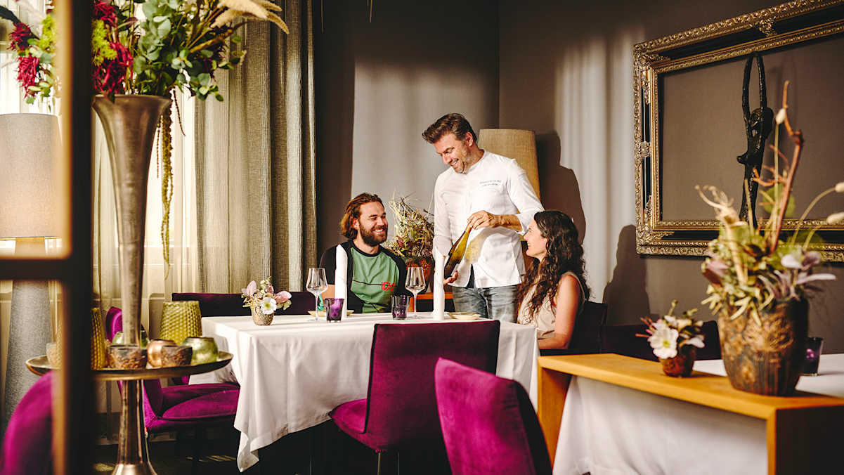 Der Spitzenkoch schenkt Wein für zwei Gäste in einem eleganten Restaurant mit gemütlicher Atmosphäre ein.