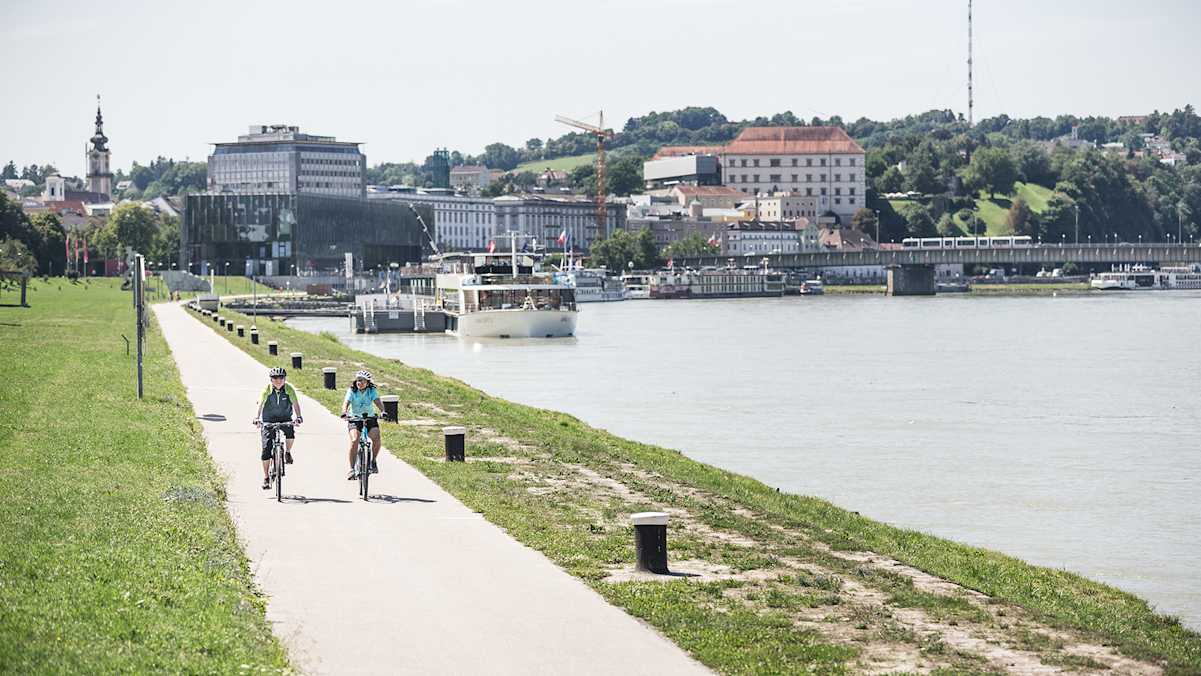 Der Donauradweg bei Linz lädt zum Radeln am Wasser mit Stadtpanorama ein.