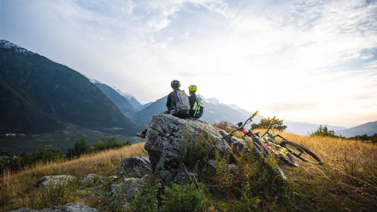Mountainbiker genießen den Ausblick am Vinschger Sonnenberg bei Sonnenuntergang.