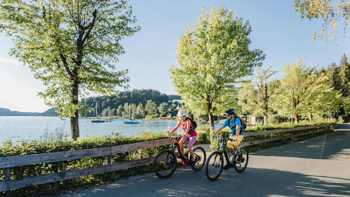 Zwei E-Biker fahren an einem See entlang.
