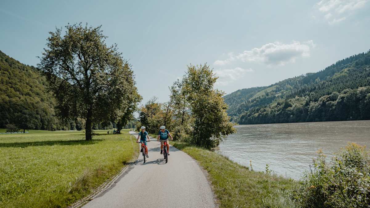 Zwei Radfahrer radeln an der Donau entlang.