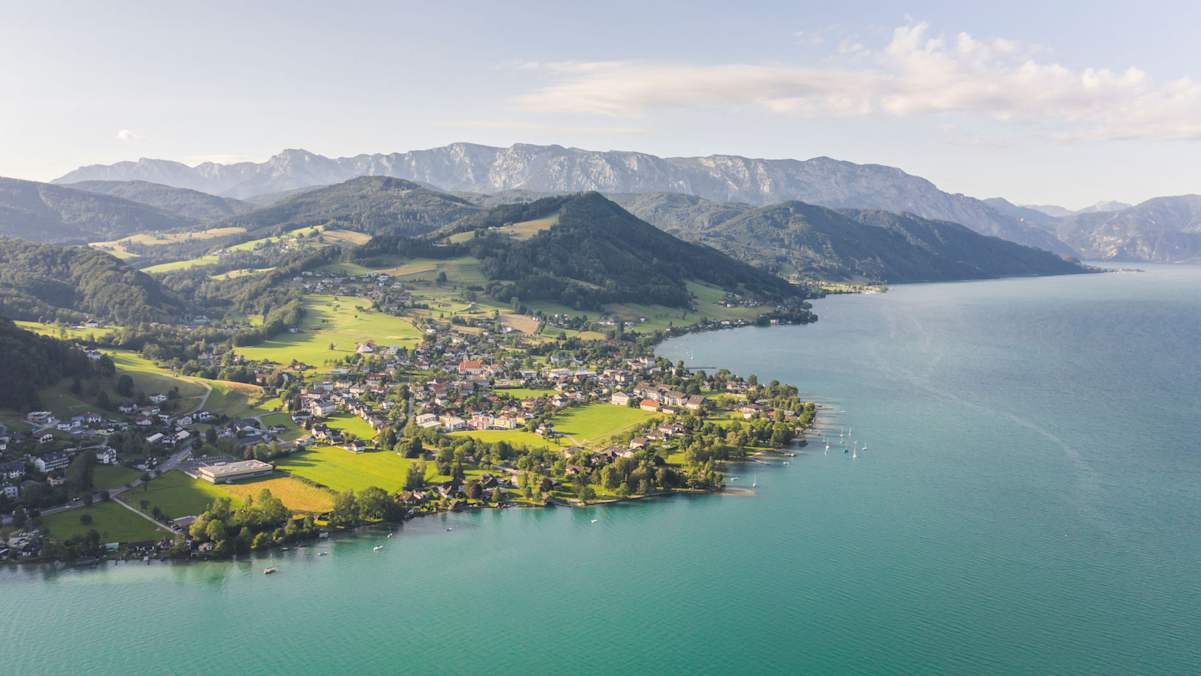 Ein kleiner Ort an einem türkisblauen See mit Bergen im Hintergrund.