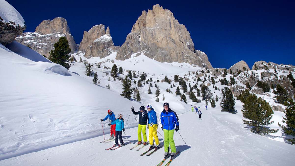 Fünf Skifahrer fahren die Sellaronda in Südtirol im Hintergrund ein schönes Dolomitenpanorama.