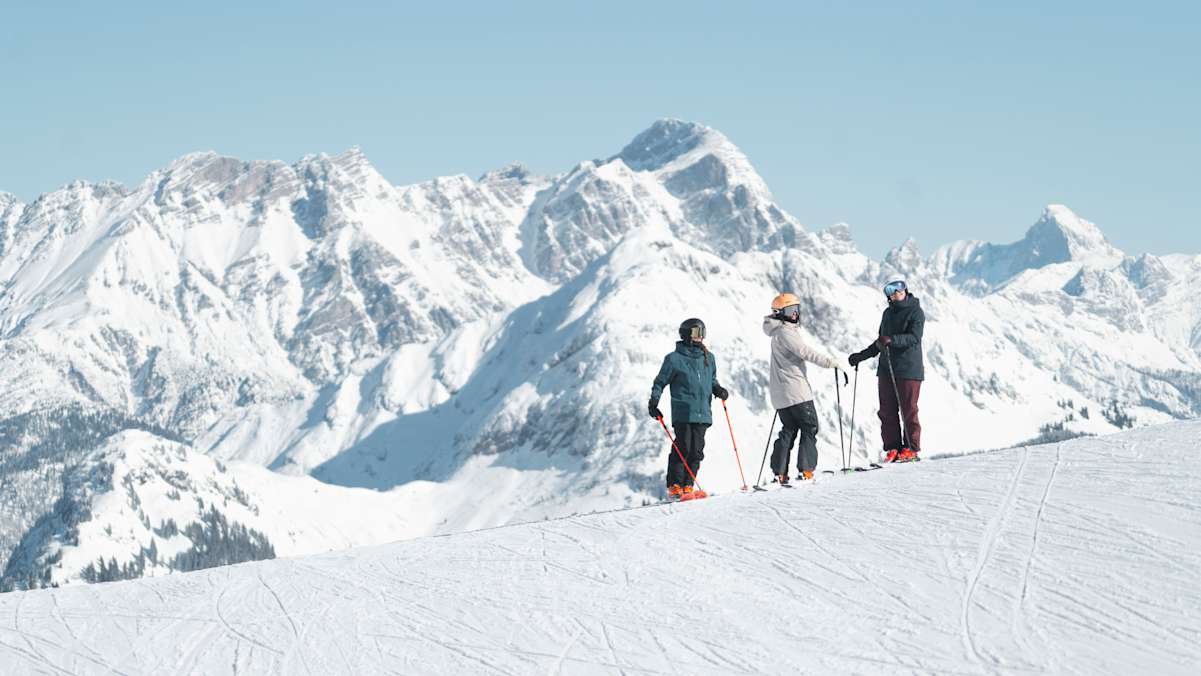 Drei Skifahrer sind im Skicircus Saalbach Hinterglemm Leogang Fieberbrunn unterwegs und blicken in die Kamera. Im Hintergrund sieht man eine verschneite Berglandschaft.