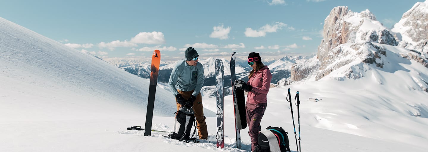 Eine Frau und ein Mann stehen im Schnee auf einem Berg und machen sich für das Skifahren bereit.
