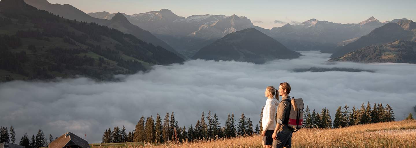 Zwei Wanderer genießen den Blick über ein Nebelmeer im herbstlichen Gstaad mit Bergpanorama im Hintergrund.