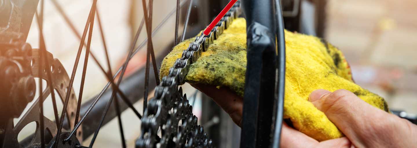 Hand die mit rotem Schlauch und gelbem Lappen eine Fahrradkette schmiert