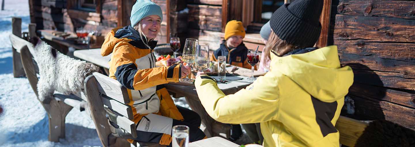 Zwei Damen stoßen mit einem Glas Wein auf der Skihütte im Winter an.