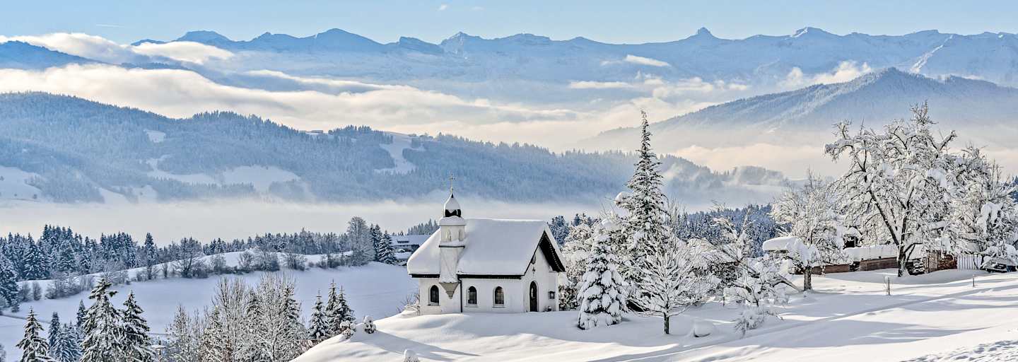 Die Hubertuskapelle in Scheidegg im Allgäu inmitten einer tief verschneiten Berglandschaft.
