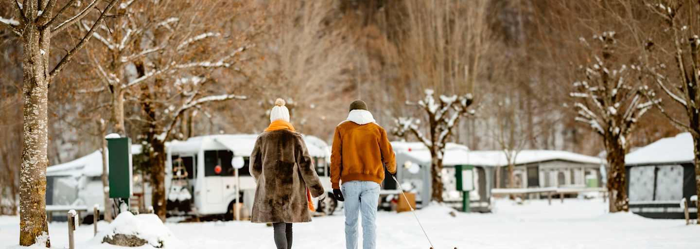 Ein Pärchen geht mit einem Rodel über einen Campingplatz im Winter.